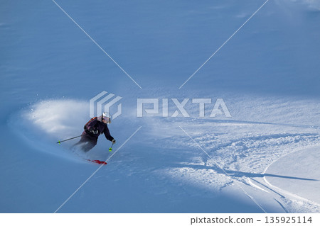 Off-piste freeride skiing in fresh powder snow with a skier carving through the slope 135925114