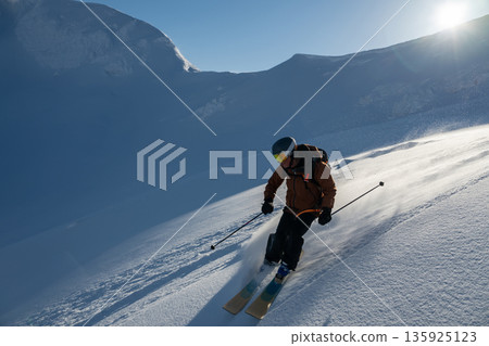 Skier carving down a sunlit powder slope on a rugged mountain during a winter adventure 135925123