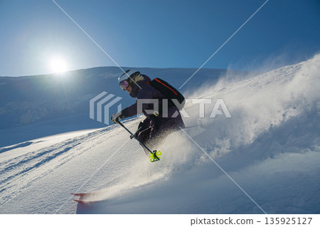 Skier in fresh powder on a sunny day carving down a mountain with backcountry gear 135925127