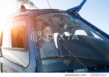 Female helicopter pilot in cockpit with headset, ready for off-piste heliskiing adventure over fresh powder snow 135925131