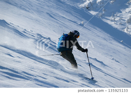 Skier carving a turn down a snowy slope with backpack in fresh powder Skier carving a turn down a snowy slope with backpack in fresh powder 135925133