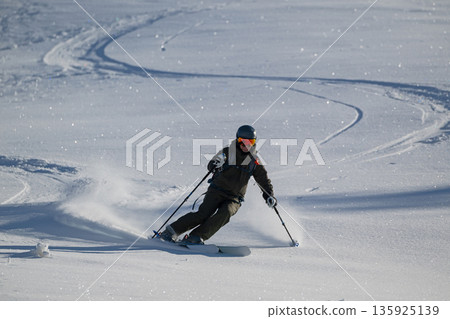 Skier carving through fresh powder on a sunlit slope with curved tracks Skier carving through fresh powder on a sunlit slope with curved tracks 135925139