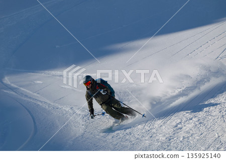 Skier carving through fresh powder off-piste on a steep Alpine slope during a sunny day 135925140