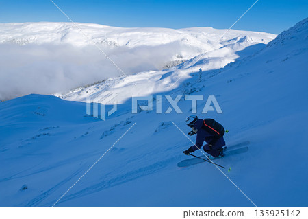Skier carving down a remote mountain slope in fresh powder with backcountry guide today Skier carving down a remote mountain slope in fresh powder with backcountry guide today 135925142