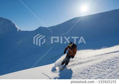 Skier carving through fresh powder on a sunlit alpine slope with dramatic mountains Skier carving through fresh powder on a sunlit alpine slope with dramatic mountains 135925155