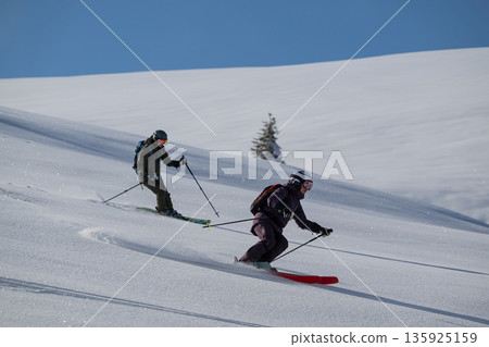 Two skiers carving through fresh powder on a sunny alpine slope in backcountry skiing 135925159