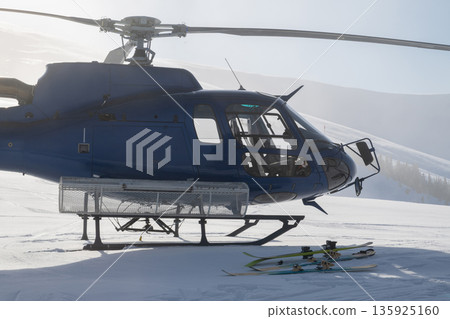 Blue helicopter on snowy mountain with skis and fresh powder in alpine landscape during sunrise 135925160