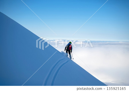 Skier on a snowy mountain ridge carving tracks in fresh powder above the clouds 135925165