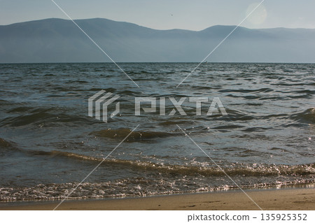 An evening view of the coastline of Vlora, Albania, taken in August 2025. Soft sunlight illuminates the rocky hills and seascape. 135925352
