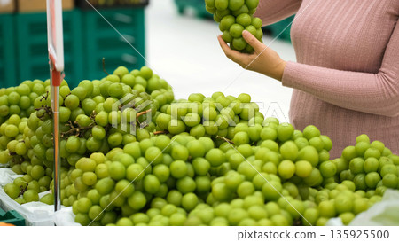 Close-up of woman selecting fresh grapes in grocery fruit section, checking freshness and color, vegan food and healthy lifestyle Close-up of woman selecting fresh grapes in grocery fruit section, checking freshness and color, vegan food and healthy lifestyle 135925500