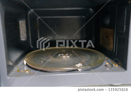 Microwave oven interior with soiled glass turntable and food residue, representing poor kitchen cleanliness, unhygienic conditions, and need for regular appliance maintenance. Microwave oven interior with soiled glass turntable and food residue, representing poor kitchen cleanliness, unhygienic conditions, and need for regular appliance maintenance. 135925828