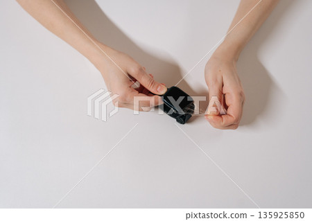 Top view of woman hands removing clear protective film from screen of dark smartwatch with fabric strap sitting at white table. Concept of device protection, repair, caring for personal technology. Top view of woman hands removing clear protective film from screen of dark smartwatch with fabric strap sitting at white table. Concept of device protection, repair, caring for personal technology. 135925850