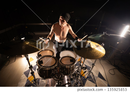 Energetic drummer performing live music with drumsticks Energetic drummer performing live music with drumsticks 135925853