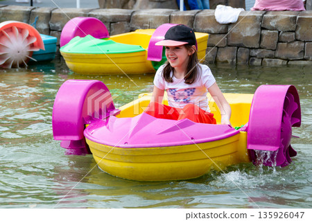 Kid playing rowing water paddle boat. Soft focus. A little girl rides a colorful boat on a pool in a resort. High quality photo 135926047