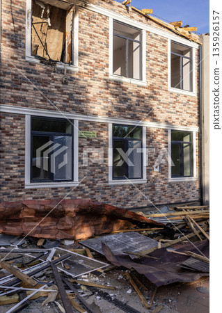 Damaged brick building with shattered windows, collapsed roof, and scattered debris; exposed interior reveals severe structural impact from destructive event. Damaged brick building with shattered windows, collapsed roof, and scattered debris; exposed interior reveals severe structural impact from destructive event. 135926157