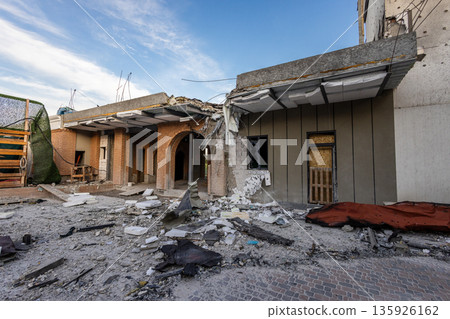 Partially collapsed building with arched brickwork, broken windows, and scattered debris; exposed wires and boarded door suggest recent destruction or ongoing repairs. Partially collapsed building with arched brickwork, broken windows, and scattered debris; exposed wires and boarded door suggest recent destruction or ongoing repairs. 135926162