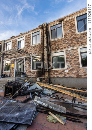 Two story brick building with charred central wall and scattered debris, including broken solar panels, marking localized fire damage. 135926167