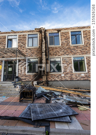 Two story brick building with charred central wall and scattered debris, including broken solar panels, marking localized fire damage. Two story brick building with charred central wall and scattered debris, including broken solar panels, marking localized fire damage. 135926168