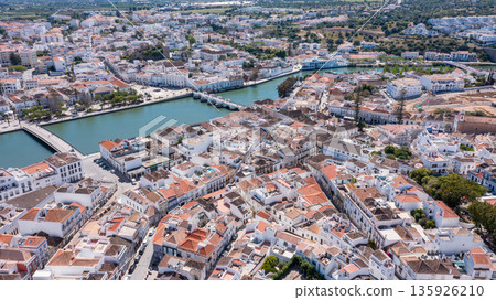 The aerial view captures Tavira with its white buildings, orange rooftops, and winding streets along the Gilao river in Algarve, Portugal on a sunny day The aerial view captures Tavira with its white buildings, orange rooftops, and winding streets along the Gilao river in Algarve, Portugal on a sunny day 135926210