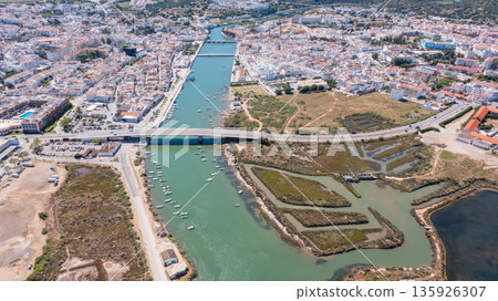 Aerial view shows Tavira, Portugal with its Gilao river, boats along the water, and buildings of the town. The scene depicts the layout and natural features 135926307