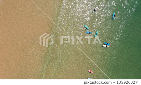 Surfers are out in the sea enjoying the waves on their surfboards. A drone captures the scene from above showing the beach and water Surfers are out in the sea enjoying the waves on their surfboards. A drone captures the scene from above showing the beach and water 135926327