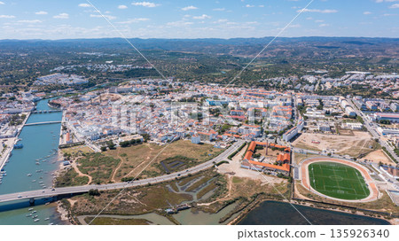 Aerial view of Tavira in Algarve highlights the rivers, roads, and buildings. The landscape shows urban areas alongside natural features and greenery Aerial view of Tavira in Algarve highlights the rivers, roads, and buildings. The landscape shows urban areas alongside natural features and greenery 135926340