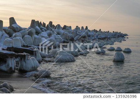 Icy breakwater on the Baltic Sea coast in Liepaja at winter sunset with frozen waves Icy breakwater on the Baltic Sea coast in Liepaja at winter sunset with frozen waves 135926396