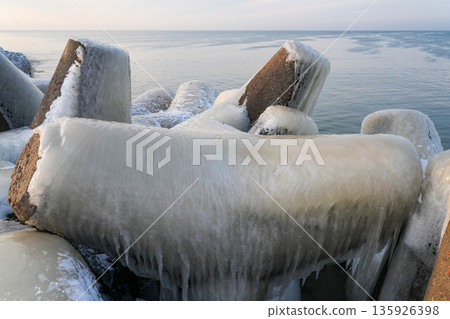 Ice-covered concrete breakwater on the Baltic Sea coast in Liepaja during a calm winter sunrise Ice-covered concrete breakwater on the Baltic Sea coast in Liepaja during a calm winter sunrise 135926398