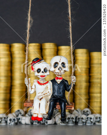 Skeleton couple on swing in front of gold coins and skulls symbolizing wealth, love, and mortality Skeleton couple on swing in front of gold coins and skulls symbolizing wealth, love, and mortality 135926410