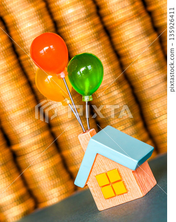 Toy house lifted by colorful balloons in front of stacked gold coins background Toy house lifted by colorful balloons in front of stacked gold coins background 135926411