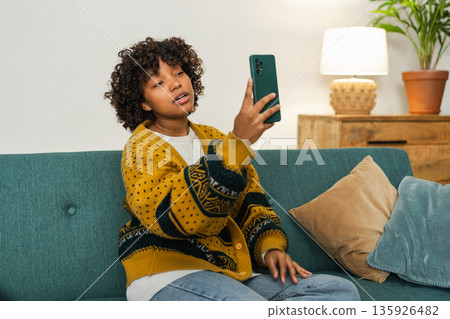African American girl holding smartphone having video chat. Female blogger chatting with best friends in social network. Young woman having virtual meeting online chat video call at home African American girl holding smartphone having video chat. Female blogger chatting with best friends in social network. Young woman having virtual meeting online chat video call at home 135926482