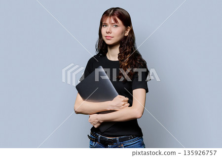 Portrait of beautiful girl teenage student holding laptop on gray background Portrait of beautiful girl teenage student holding laptop on gray background 135926757