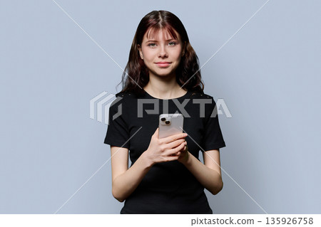 Portrait of female high school student with smartphone on gray background Portrait of female high school student with smartphone on gray background 135926758