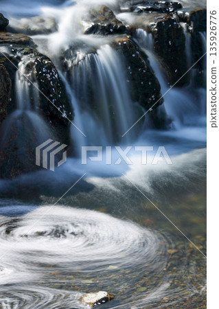 Cherry blossoms flowing between rocks and a small waterfall_Vertical Cherry blossoms flowing between rocks and a small waterfall_Vertical 135926776