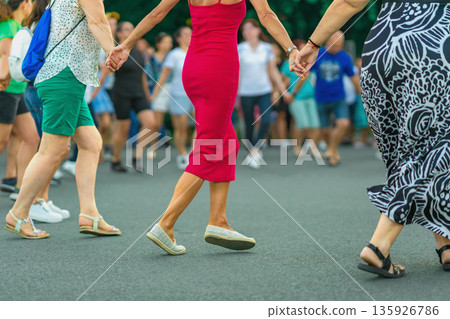 People dancing Bulgarian horo folk dance. Group of people holding hands and dancing traditional Bulgarian horo outdoors. Cultural event, folk dance, community, heritage, tradition People dancing Bulgarian horo folk dance. Group of people holding hands and dancing traditional Bulgarian horo outdoors. Cultural event, folk dance, community, heritage, tradition 135926786
