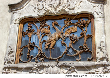 Ornate historic window with carved wooden stork ornament on old building facade 135926997