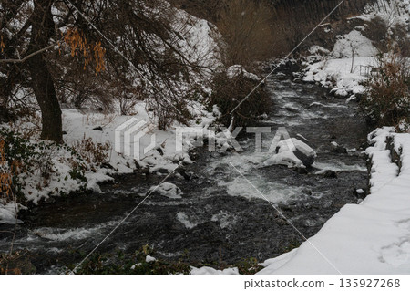 Winter river flows through snow-covered banks beneath rocky cliffs at the Symphony of Stones, dark moving water contrasts with white snow Winter river flows through snow-covered banks beneath rocky cliffs at the Symphony of Stones, dark moving water contrasts with white snow 135927268