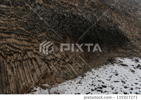 Basalt columns curve into dramatic rock wall at Symphony of Stones, volcanic formations create layered textures contrasting with snow-covered ground Basalt columns curve into dramatic rock wall at Symphony of Stones, volcanic formations create layered textures contrasting with snow-covered ground 135927271