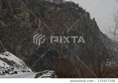 Towering basalt cliffs rise above a snow-covered road at the Symphony of Stones, vertical volcanic columns dark rock textures contrast Towering basalt cliffs rise above a snow-covered road at the Symphony of Stones, vertical volcanic columns dark rock textures contrast 135927298