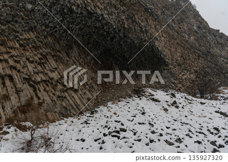 Basalt columns curve into dramatic rock wall at Symphony of Stones, volcanic formations create layered textures contrasting with snow-covered ground Basalt columns curve into dramatic rock wall at Symphony of Stones, volcanic formations create layered textures contrasting with snow-covered ground 135927320