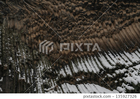 Vertical basalt columns create dense geometric textures at Symphony of Stones, dark volcanic rock contrasts with scattered snow 135927326