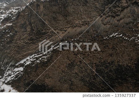 Towering basalt columns form a rugged cliff face at Symphony of Stones, snow-dusted textures and layered rock patterns create dramatic winter scene 135927337