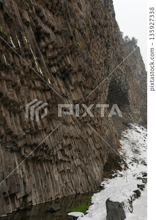 Vertical basalt columns rise above narrow river at Symphony of Stones, dark volcanic rock textures contrast with snow, flowing water in winter light Vertical basalt columns rise above narrow river at Symphony of Stones, dark volcanic rock textures contrast with snow, flowing water in winter light 135927338