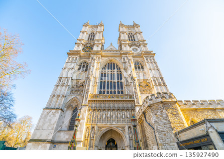 Westminster Abbey stands tall in London. The grand structure shows its detailed facade and towers. Visitors admire the historic site in the sunlight, capturing its notable features. 135927490