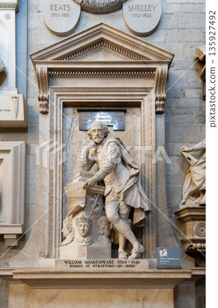 A memorial statue of William Shakespeare stands in Westminster Abbey in London. It shows him with a scroll. Visitors come to pay their respects and admire the artwork. 135927492