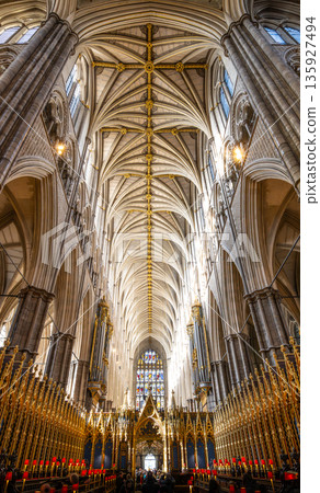 Visitors walk under the tall ceilings of Westminster Abbey in London. The light shines through tall windows, highlighting the intricate design. This location hosts many important events. 135927494
