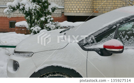 A car and a tree behind it near the brick wall are covered in snow after a snowfall. White Car Covered in Snow Parked Near House A car and a tree behind it near the brick wall are covered in snow after a snowfall. White Car Covered in Snow Parked Near House 135927514