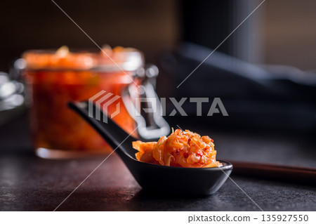 Fermented cabbage. Kimchi. Korean food in ceramic spoon on black table. Fermented cabbage. Kimchi. Korean food in ceramic spoon on black table. 135927550