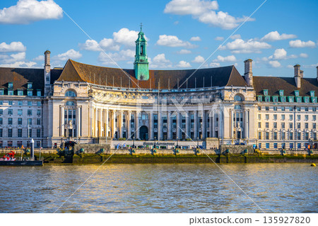 County Hall is located along the River Thames in London. The building has a large facade and a clock tower. People often visit this area to enjoy the view and surroundings. County Hall is located along the River Thames in London. The building has a large facade and a clock tower. People often visit this area to enjoy the view and surroundings. 135927820
