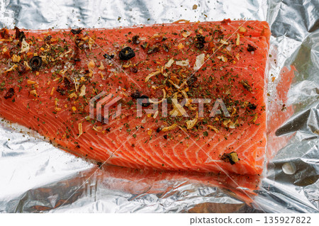 Top view of a raw salmon fillet seasoned with herbs and spices on aluminum foil, prepared for oven cooking. 135927822